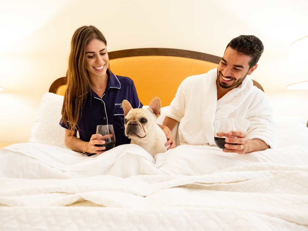 Couple In Bed With Their Dog And Wine.