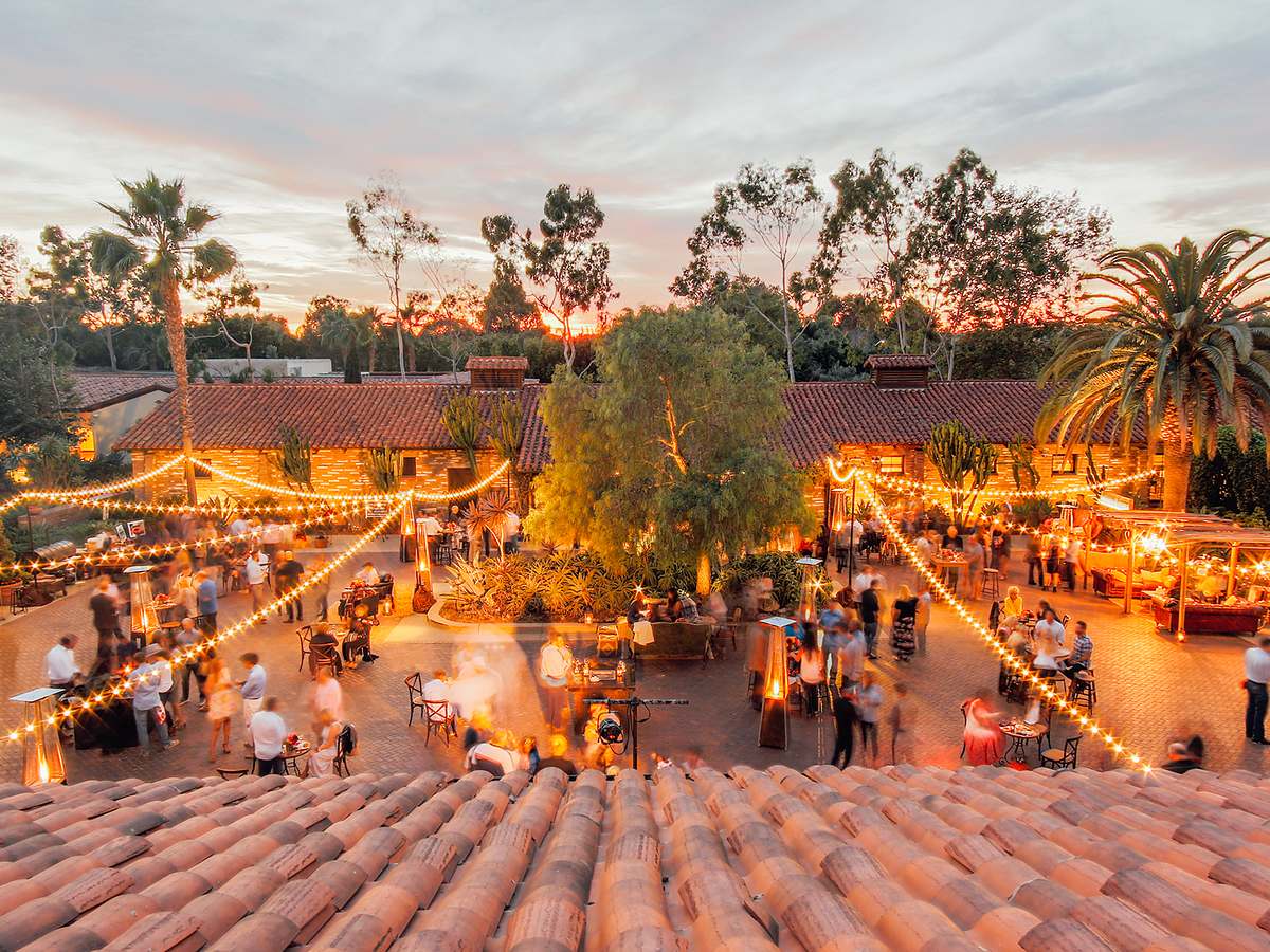 Twinkling string lights illuminate a Spanish hacienda-style courtyard at dusk as guests gather for an evening event at Estancia La Jolla Hotel & Spa in La Jolla, California.
