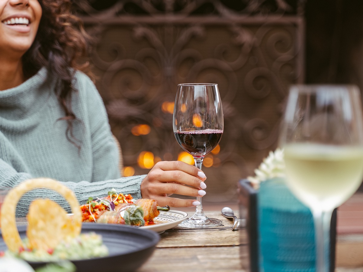 Guest enjoying red wine and bacon-wrapped appetizers by the fireside patio at Estancia La Jolla Hotel & Spa in La Jolla, California