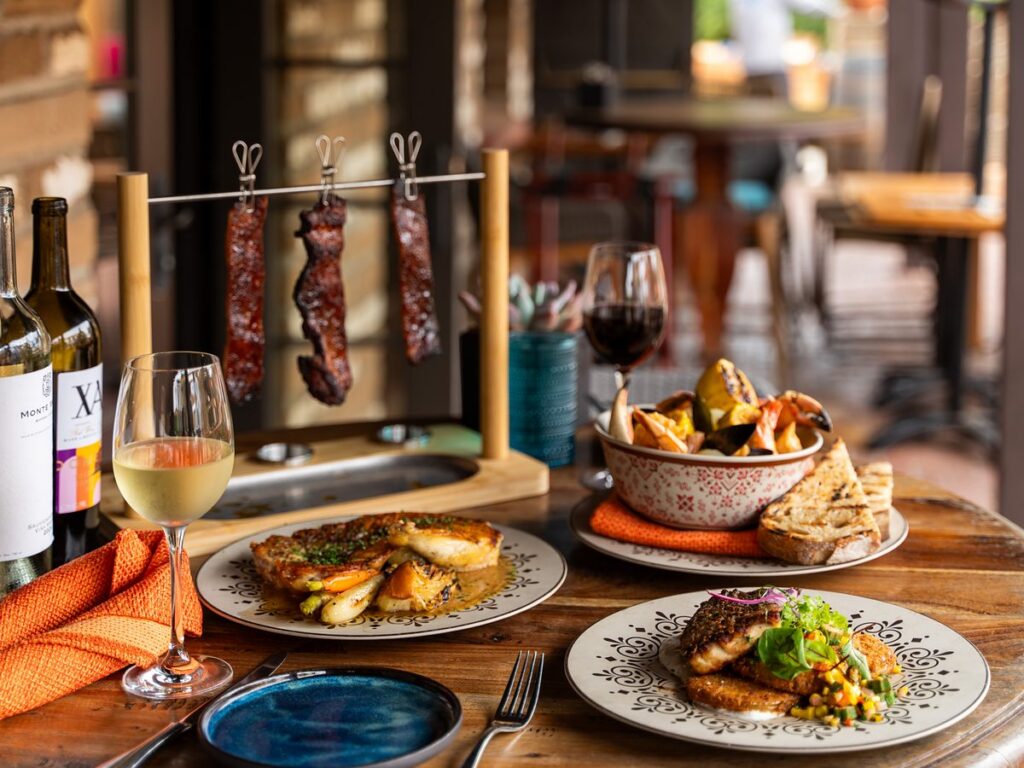 Signature hanging glazed ribs above a plated entrée at Estancia La Jolla restaurant in La Jolla, California, styled on hand-painted ceramic with grilled bread and wine.