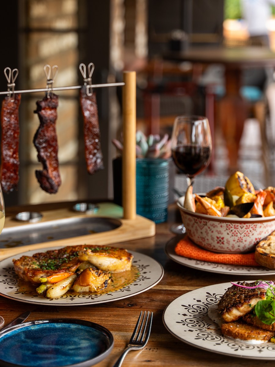 Signature hanging glazed ribs above a plated entrée at Estancia La Jolla restaurant in La Jolla, California, styled on hand-painted ceramic with grilled bread and wine.
