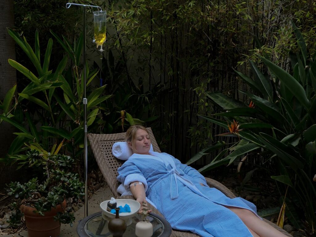 Guest relaxing in a blue robe during an IV wellness drip therapy treatment in the tropical garden at Estancia La Jolla Hotel & Spa in La Jolla, California