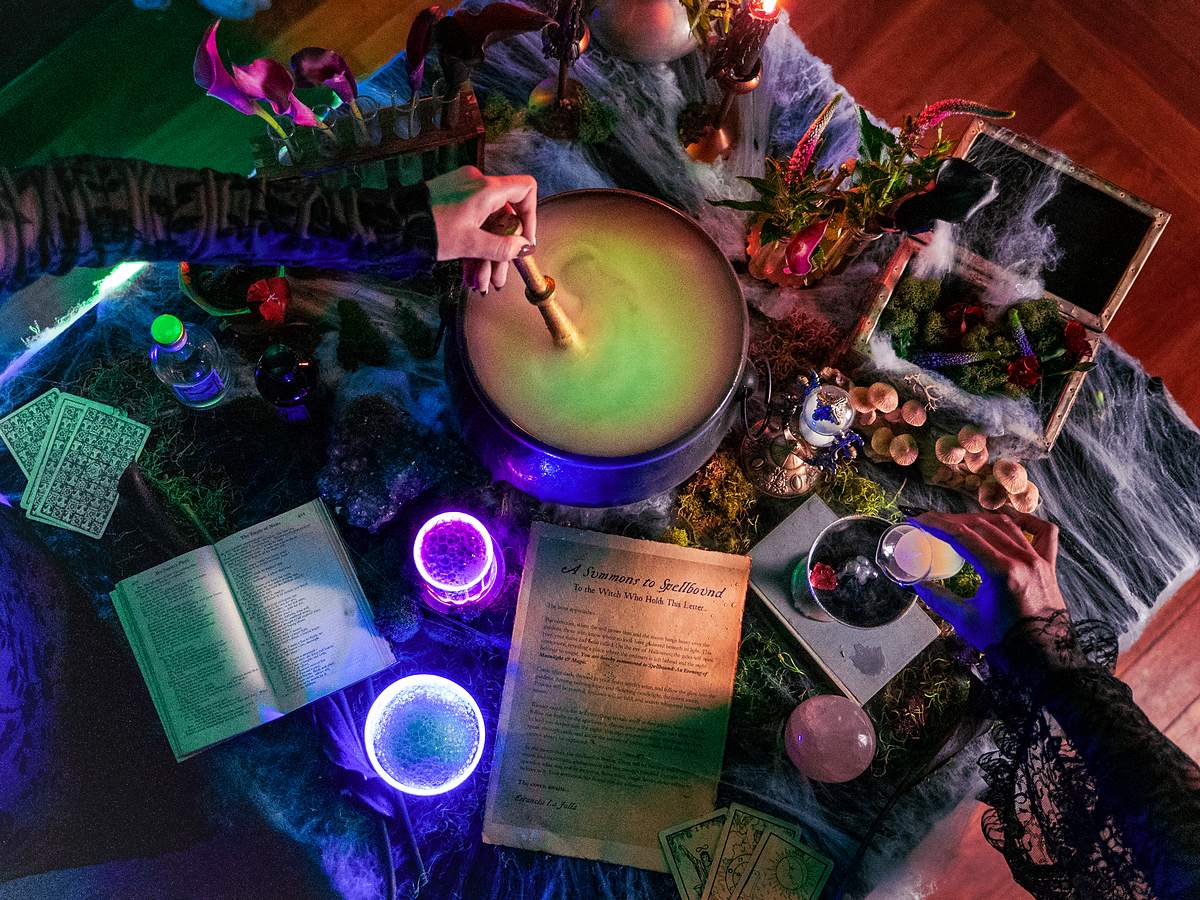 Glowing witch's cauldron surrounded by tarot cards, candles and apothecary potions at the Spellbound Halloween event at Estancia La Jolla Hotel & Spa in La Jolla, California
