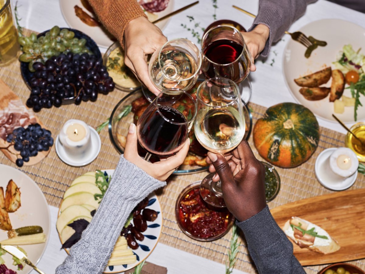 Friends raising red and white wine glasses in a toast over a festive Thanksgiving dinner table with grapes, charcuterie, and a fall pumpkin at Estancia La Jolla Hotel & Spa in La Jolla, California